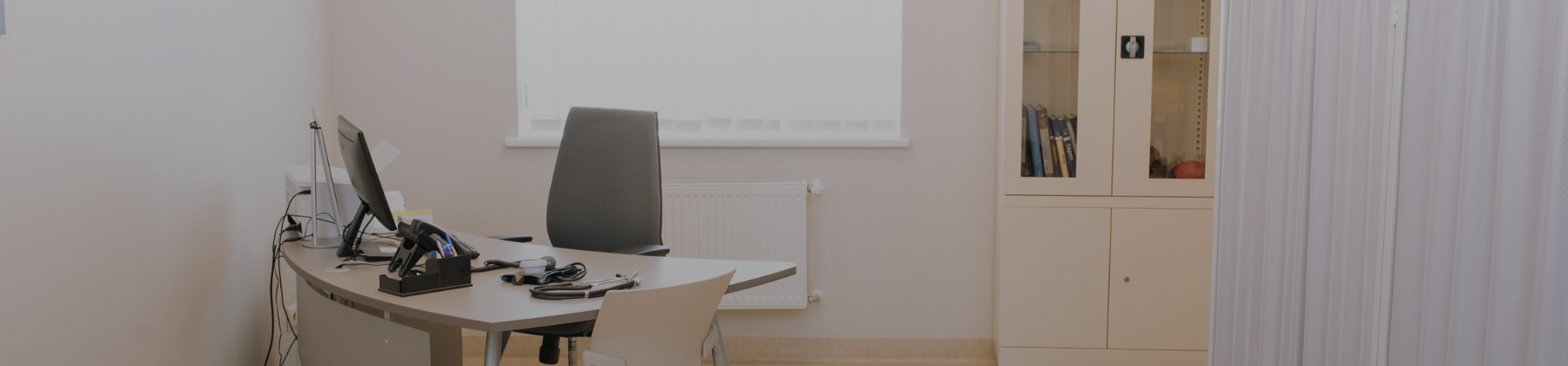 Minimal medical clinic consultation room with desk, chair, computer and storage cabinets, representing a professional cosmetic or healthcare setting.